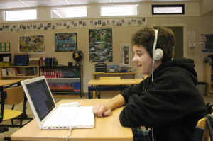 teen wearing headphones and sitting in front of a computer. 