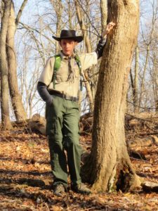 Seth in his boy scout uniform standing in the woods by a tree.