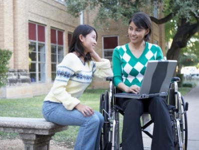 A student in a wheel chair talking with a student sitting on a bench.
