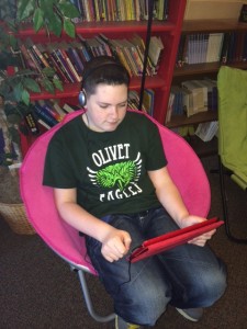 Carson sitting in a pink chair with headphones reading a book on his iPad with Read2Go app.