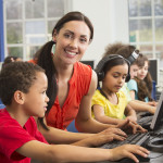 Teacher working with young students who are wearing headphones and reading digital accessible books on their computers.