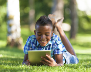 Boy reading on a tablet sitting on the grass
