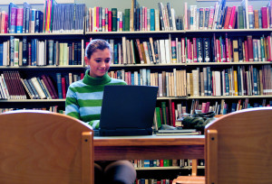 Female student in library reading a digital book on a computer