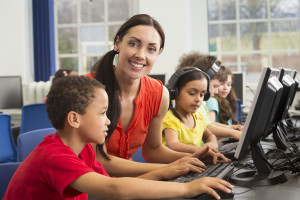 Teacher with young students using computers with headphone