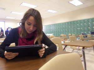 Emeline reading on her tablet in a school room.
