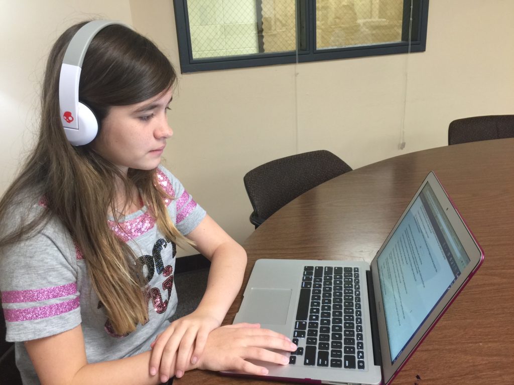Alyssa Campbell reading a book from Bookshare on her computer with headphones. 