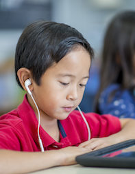A young boy wearing earphones reads a book on a tablet