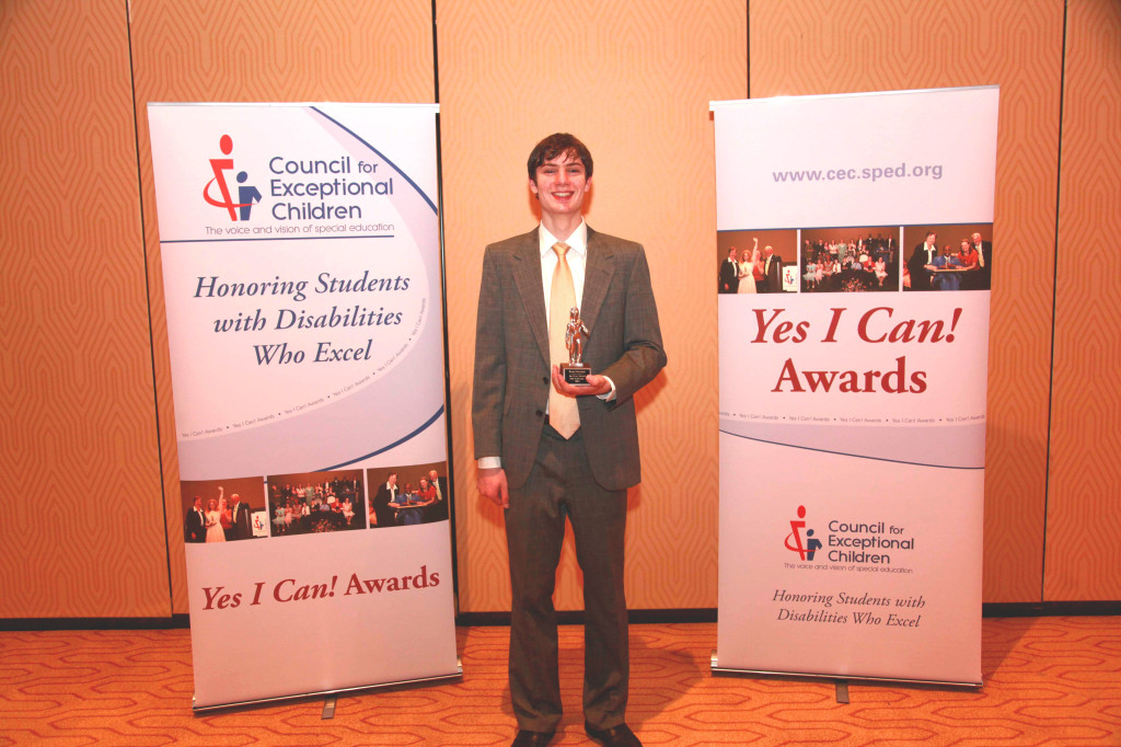 Brian Meersma is standing on a stage and holding an award for students with disabilities who excel.
