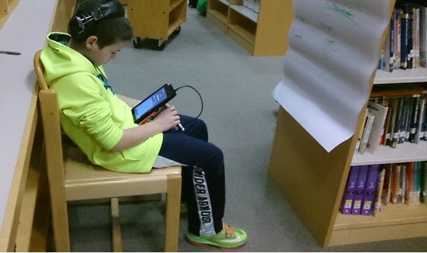 a boy is reading and listening to a book on a tablet while sitting in the library