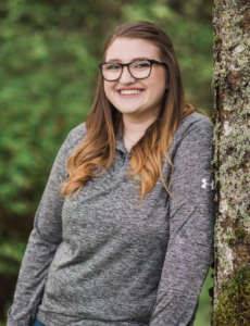 LenaMarie is smiling and leaning against a tree