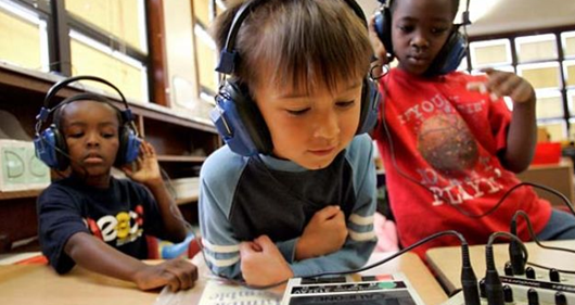 three students are wearing headphones and reading tablets in a classroom