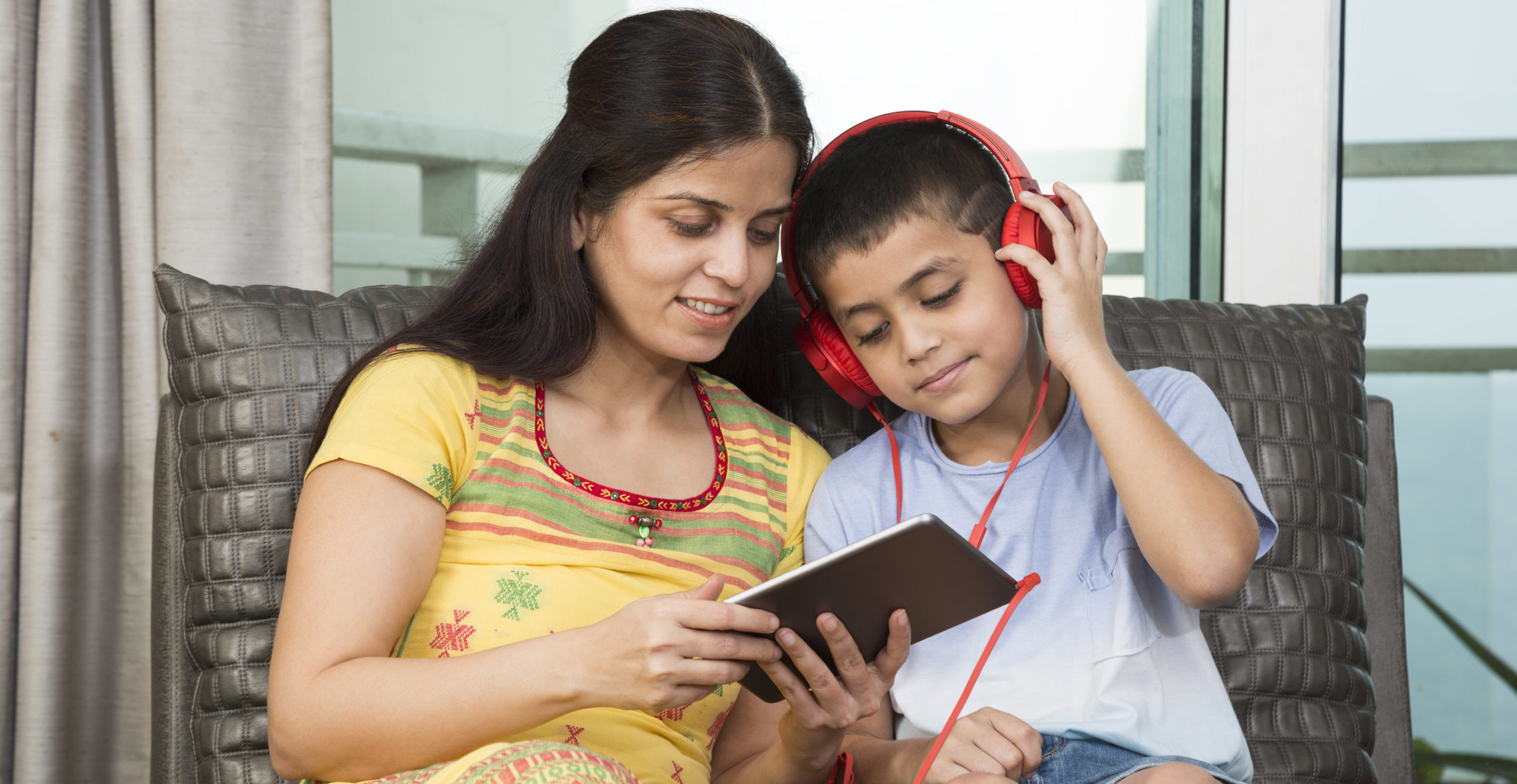 Mother and son read on a tablet with son wearing headphones
