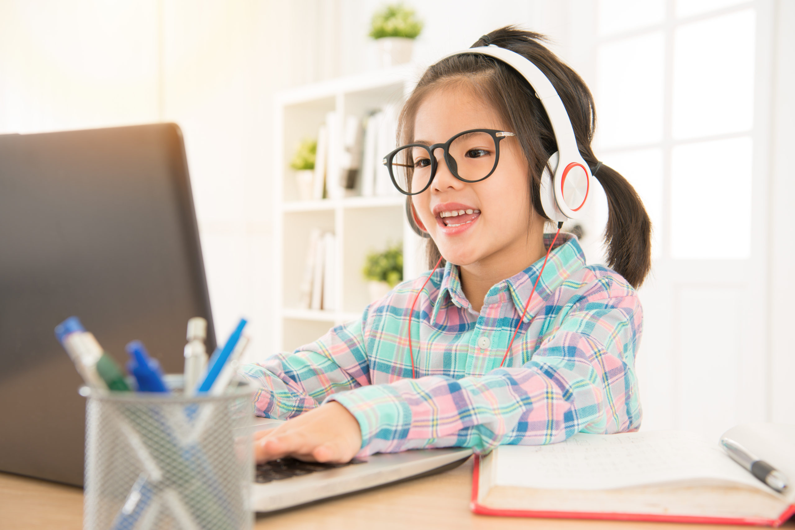 young girl is wearing glasses and headphones while using a computer
